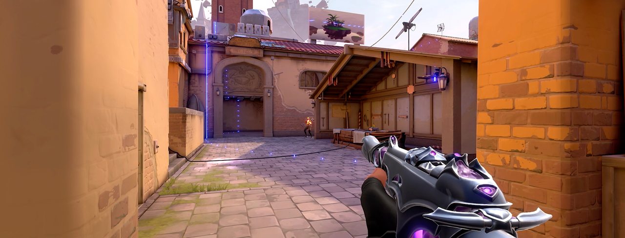 A first-person view down a sunny street on a VALORANT map
